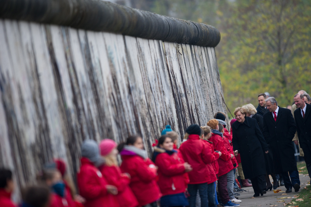 German Chancellor Angela Merkel, left, shakes hands with children symbolizing so-called Mauerspechte (wall peckers – people who chipped the wall with hammers) along remains of the Berlin Wall at the Berlin Wall memorial site at Bernauer Strasse in Berlin, Germany on Sunday.