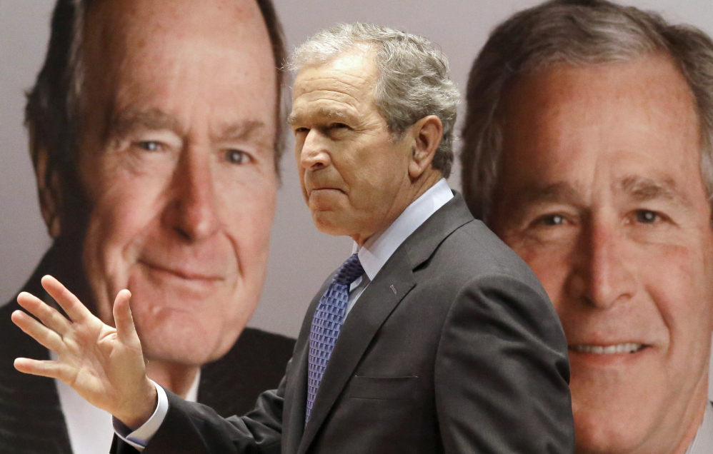 Former President George W. Bush passes by a portrait of himself and his father former President George H.W. Bush as he takes the stage to discuss his new book, “41: A Portrait of My Father” at the his father’s presidential library Tuesday in College Station, Texas.