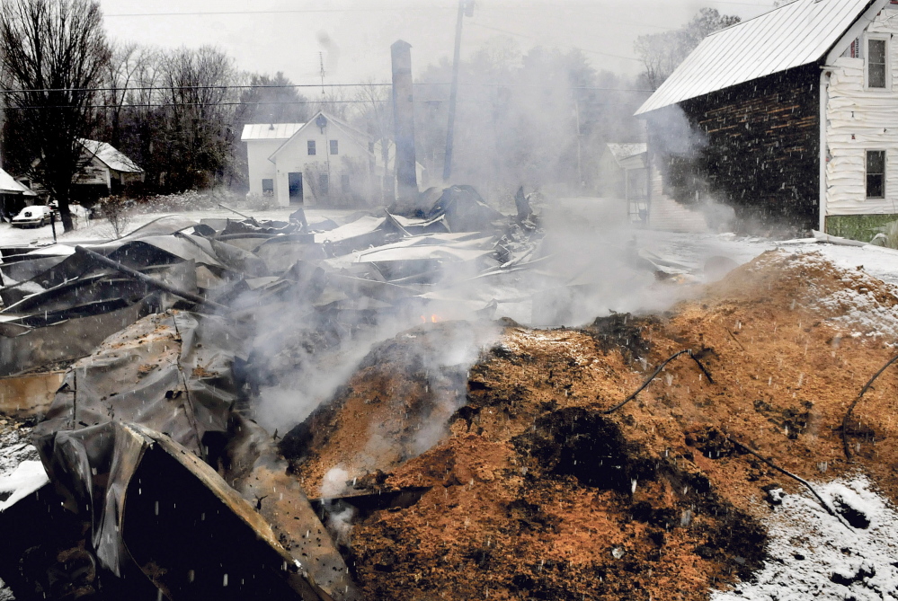Smoke and flames rise from a large pile of pellets behind the home of Rick and Tina Belanger on Monday hours after fire destroyed their Main Street home in Caratunk. In the background is the home of Dan and Marie Beane who own the post office property and called in the fire.
