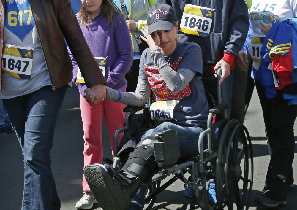 In this April 19, 2014, file photo, Boston Marathon bombings survivor Rebekah Gregory DiMartino wipes tears as she is led in her wheelchair after crossing the finish line of the Boston Marathon Tribute Run in Boston.