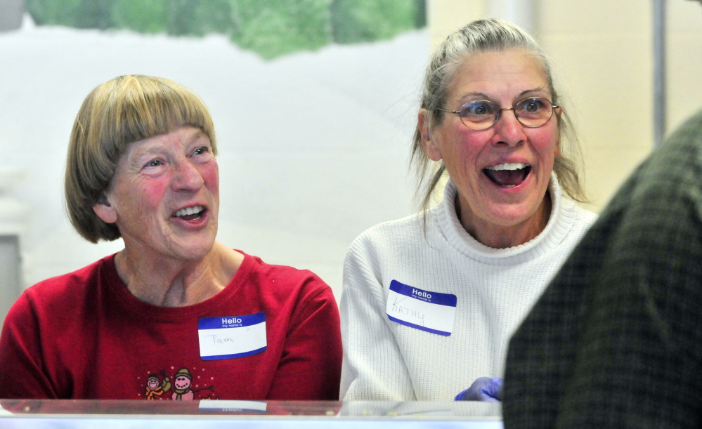 Volunteers Pam Amerin, left, and Kathy Ouellette chat with a person in the food line as they serve up a community Thanksgiving dinner Thursday at Gardiner Area High School.