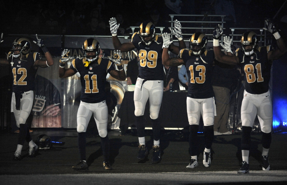 Members of the St. Louis Rams raise their arms in awareness of events in Ferguson, Mo., before Sunday’s NFL game against the Oakland Raiders.