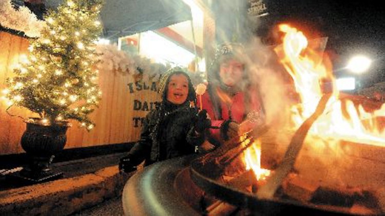 Christina Easler, right, and her son Gavyn, 4, toasted a marshmallow over an open fire on Water Street at the Parade of Lights on Water Street in downtown Skowhegan last December. The annual event returns this weekend, one of a number of events planned in the region as the holiday season moves into full swing.