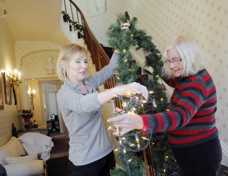 Debbie Sherman, right, takes holiday lights from Tammy Costigan on Tuesday while wrapping garland on the stairs of the Blaine House with other members of the Kennebec Valley Garden Club.
