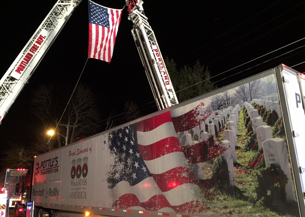 A tractor-trailer filled with balsam wreaths passes under an American flag outside Cheverus High School in Portland on Sunday.