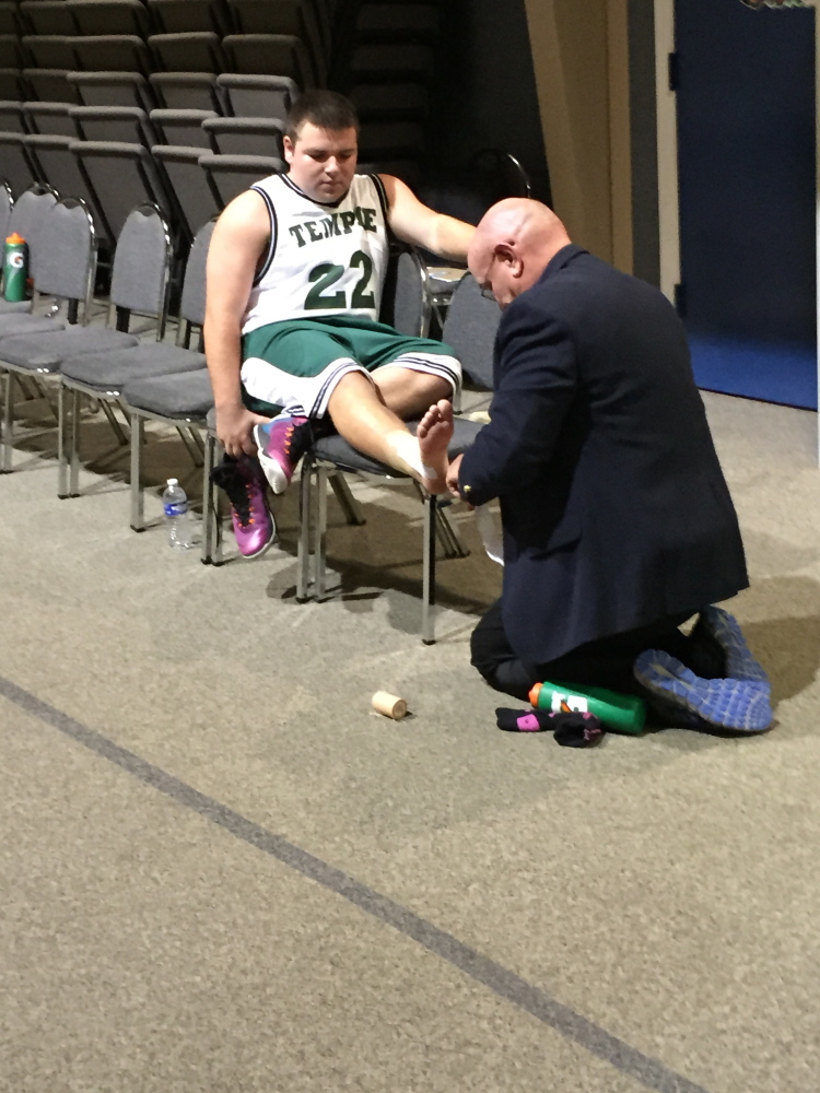 Temple boys basketball coach Tom Simmons tapes an ankle of junior Tristan Richards before a game Monday against Greater Portland Christian.