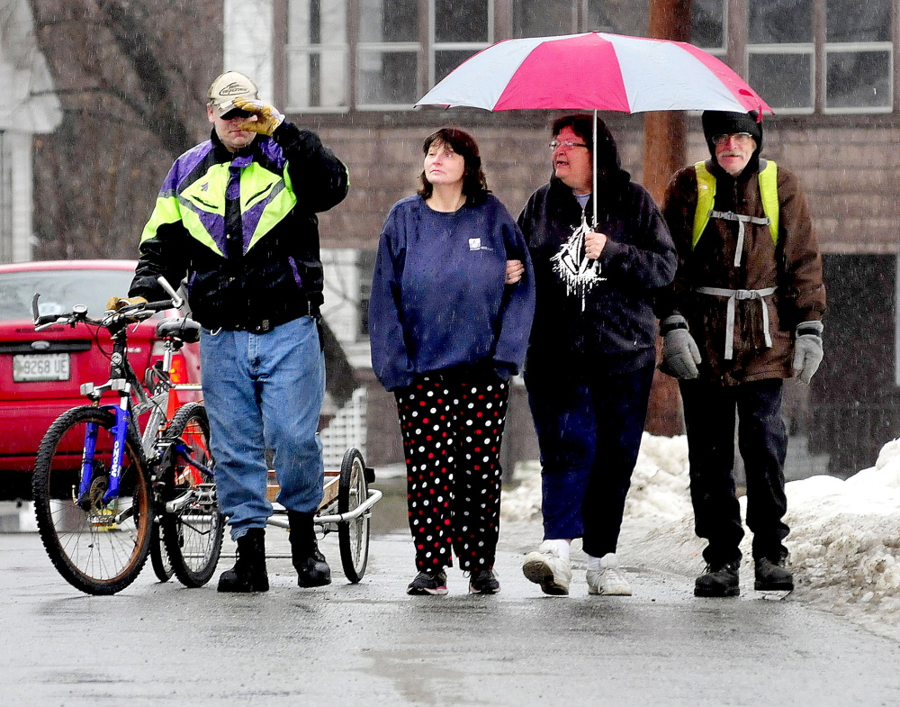 Doug Whitney, with bike, and Lisa Douglass, and Betsy and Francis Dittman share an umbrella in the rain in Waterville on Wednesday.