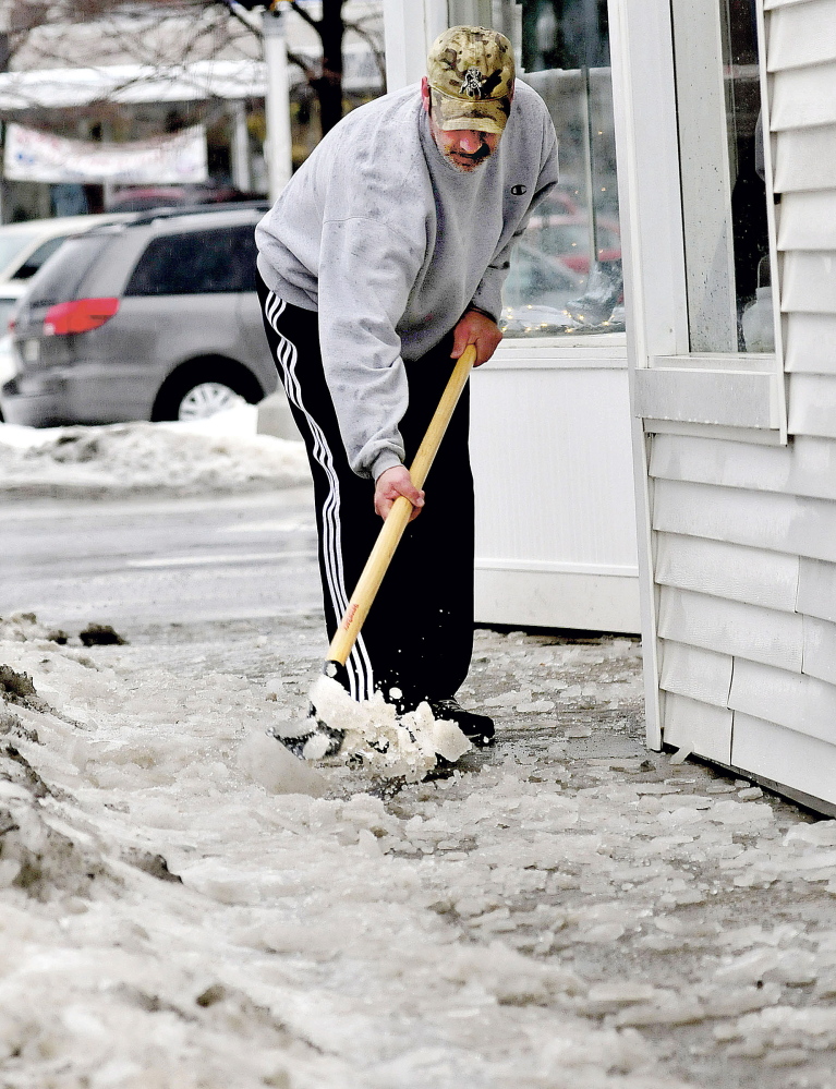 Lee Poulin uses a chisel to chop ice covering sidewalks in Waterville on Wednesday.