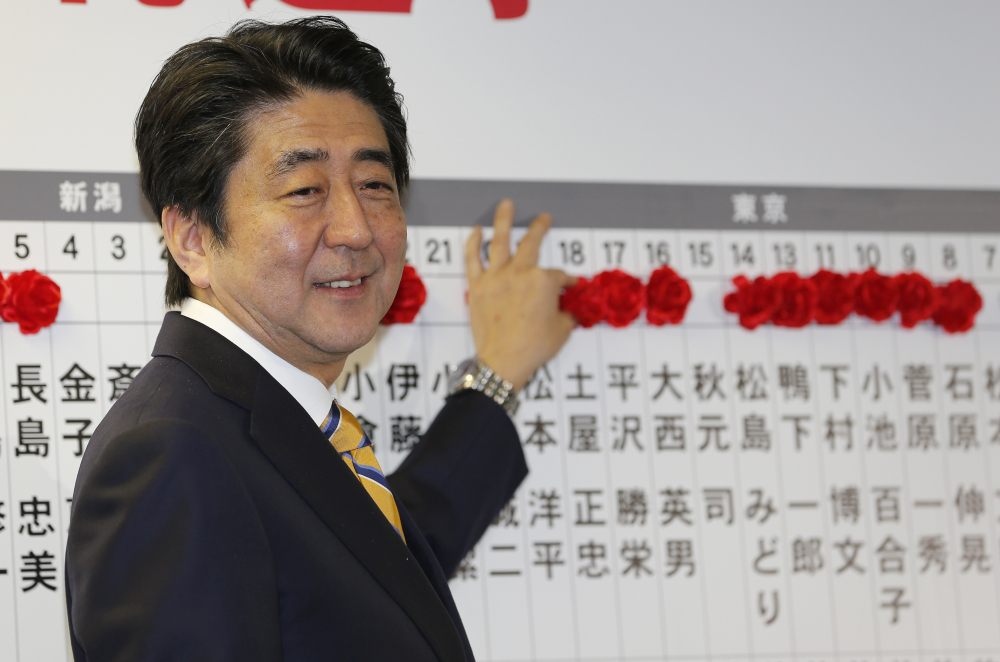 Japanese Prime Minister Shinzo Abe, leader of the Liberal Democratic Party, smiles as he places a red rosette on the name of his Liberal Democratic Party’s winning candidate during ballot counting for the lower house elections at the party headquarters in Tokyo on Sunday.