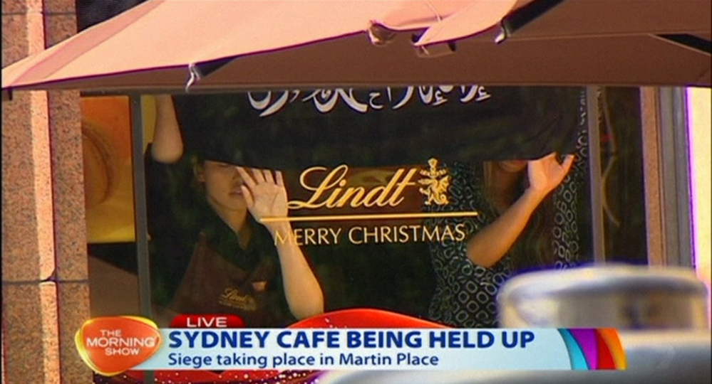 This image taken from video shows people holding up what appeared to be a black flag with white Arabic writing on it, inside a cafe in Sydney, Australia Monday.