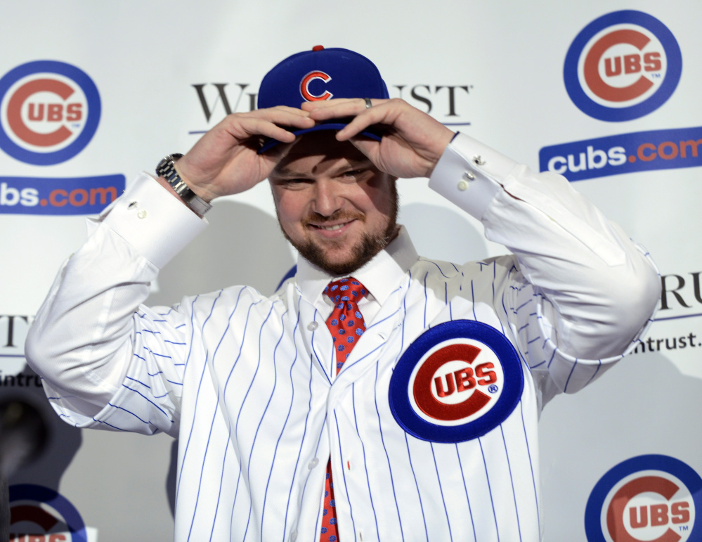 Pitcher Jon Lester puts on a Chicago Cubs jersey and hat after being introduced as a member of the Chicago Cubs baseball team during a news conference in Chicago on Monday. Lester agreed to a $155 million, six-year contract with the Cubs at the winter meetings last week that set baseball records for largest signing bonus and biggest upfront payment.