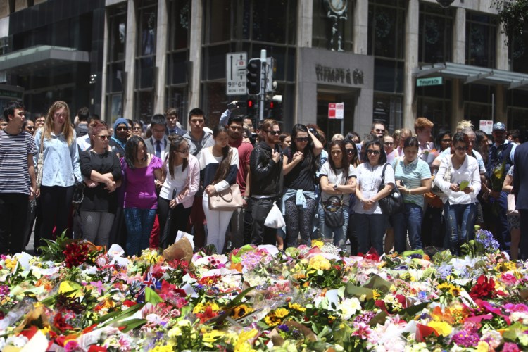 Staff members from the Lindt Chocolat Cafe with their arms linked pay tribute to their colleague who lost his life during a siege at the popular coffee shop at Martin Place in the central business district of Sydney, Australia, Tuesday.