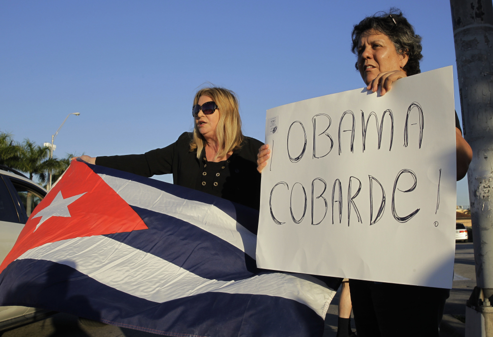 Ana Lourdes Cuesta, left, and Liliana Cuerra, of Miami, protest in Miami, Wednesday, Dec. 17, 2014, the Obama administration's decision to re-establish diplomatic relationships with Cuba. Cuerra holds a sign that reads "Obama coward." (AP Photo/Marta Lavandier)