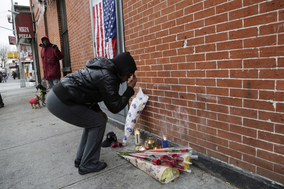 Maria Alomar genuflects Sunday at a makeshift memorial for the two police officers who were shot there Saturday, in the Bedford-Stuyvesant neighborhood of Brooklyn. Alomar’s niece is an NYPD crime scene investigator. “It could have been her in the car,” she said.
