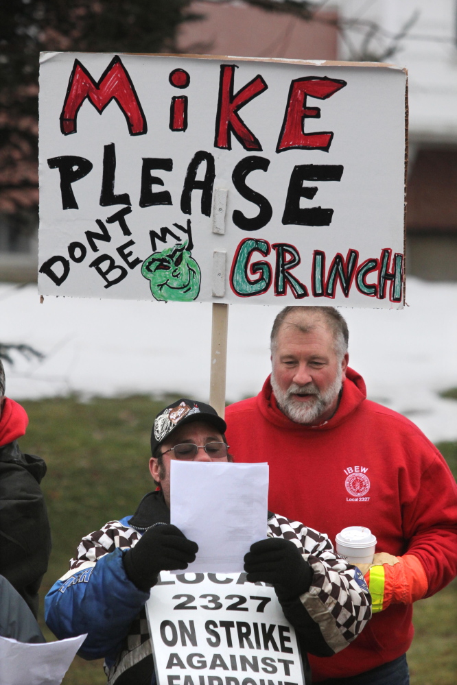 Jim Feeney Jr. of Carmel looks over the shoulder of a fellow striking FairPoint worker while singing Christmas carols outside the Winslow home of Mike Reed, state president for FairPoint in Maine, on Tuesday.