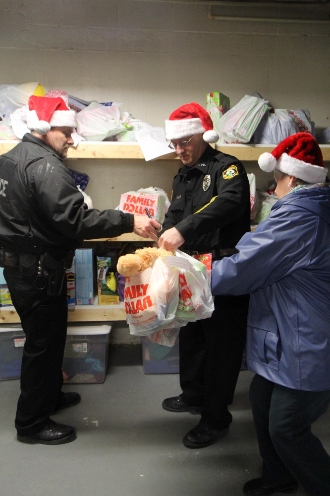 Fairfield police Officers Matthew Wilcox, left, and William Beaulieu, center, along with volunteer Marlene Angers, organize Christmas presents to be delivered to local families on Tuesday night in Fairfield.