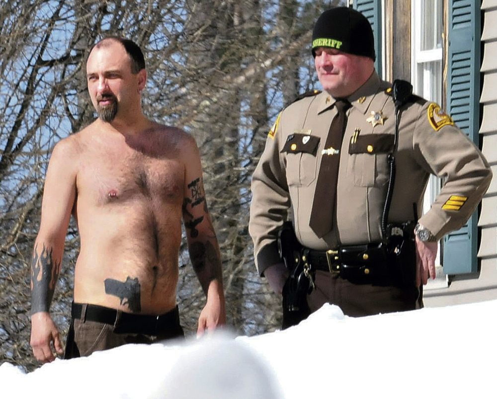 Michael Smith, left, bearing a realistic-looking tattoo of a handgun on his stomach, stands beside a Somerset County Sheriff deputy outside his home in Norridgewock, Maine on March 18. Smith was arrested June 13 after he allegedly showed up at a deputy’s home with a real gun in his waistband and drugs in his backpack. He was charged with stealing prescription narcotics from his girlfriend and released from the Somerset County Jail on $1,000 cash bail.