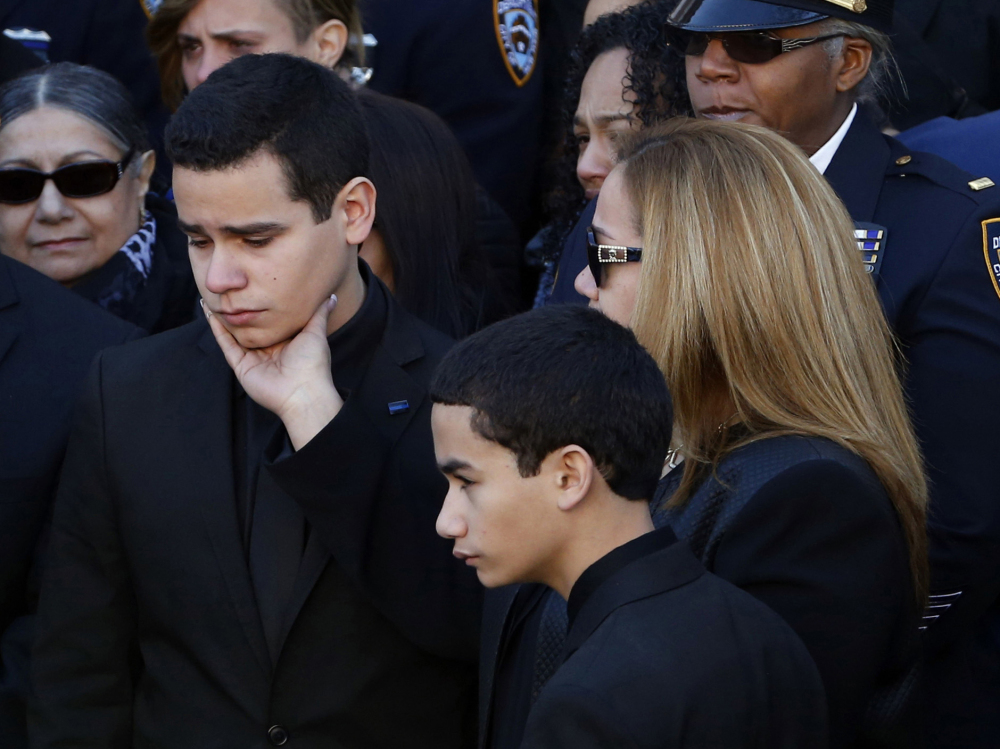 Justin Ramos, the son of slain New York City police officer Rafael Ramos, left, is comforted by his mother, Maritza Ramos, following funeral services at Christ Tabernacle Church, in the Glendale section of Queens, Saturday, Dec. 27, 2014, in New York. Also pictured is officer Ramos’ other son, Jaden Ramos, bottom.