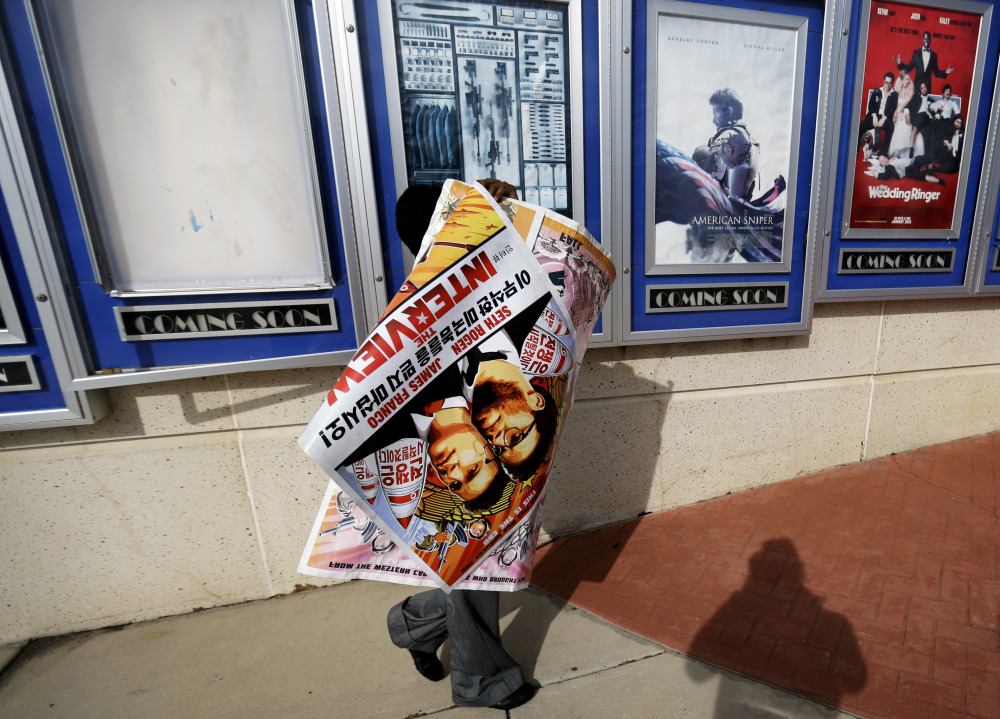 A worker carries away a poster for the movie “The Interview” after pulling it from a display case at a Carmike Cinemas movie theater in Atlanta on Wednesday. The Associated Press