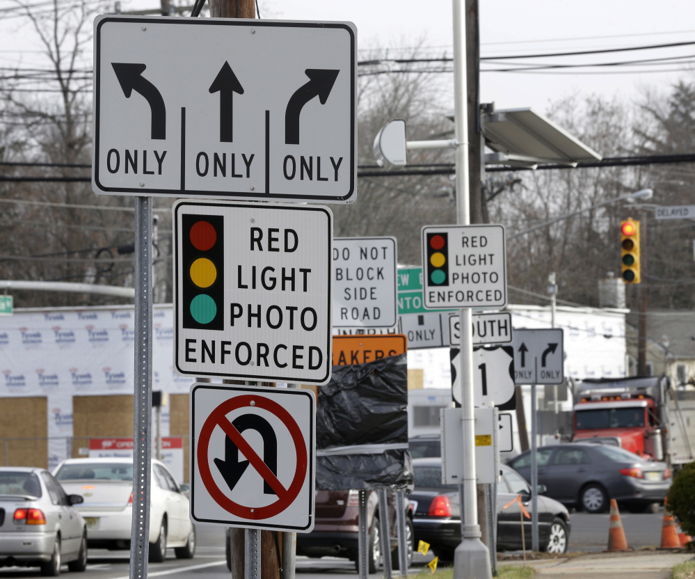 Traffic passes a photo enforcement sign below a red-light camera in Lawrence Township, N.J.  The Associated Press