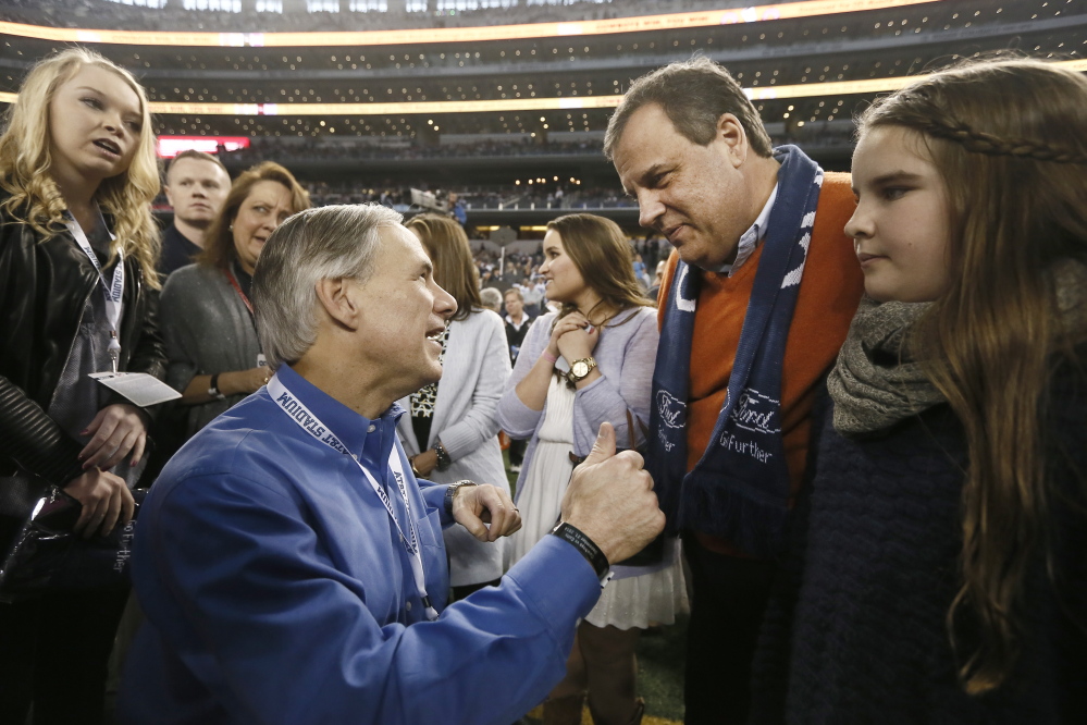 Texas Gov.-elect Greg Abbott, left, speaks with New Jersey Gov. Chris Christie, right, before a game between the Dallas Cowboys and Indianapolis Colts in December in Arlington, Texas. Christie has brushed off criticism that he has attended several games on the tab of the team owner.