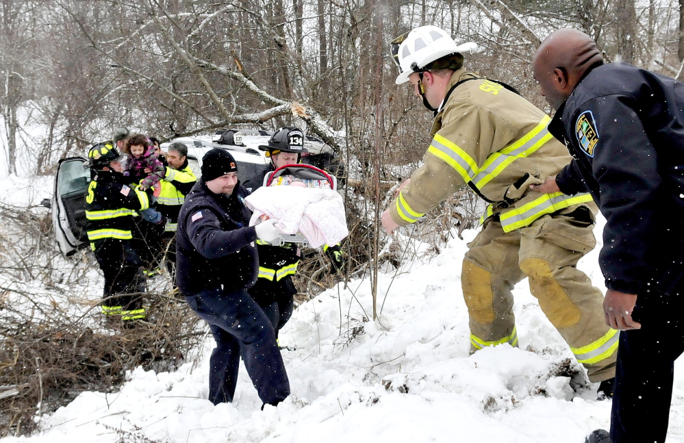 Skowhegan police and firefighters pass one of two infants up an embankment after  the car they were riding in that slid off the Norridgewock Road in Skowhegan on Monday. Two other older children also escaped the crash apparently unhurt.