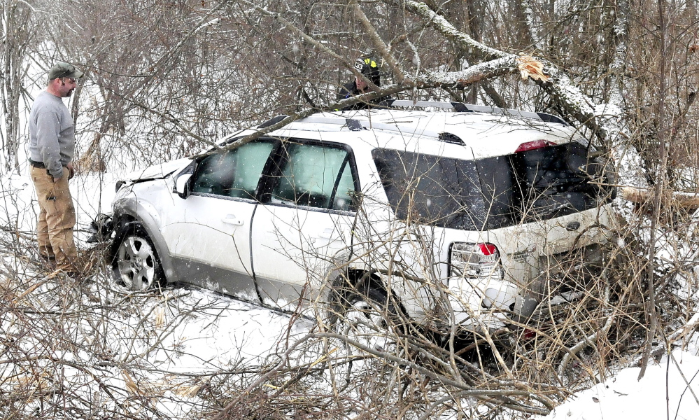 A Skowhegan firefighter, background,  looks inside the vehicle that slid off the snow-covered Norridgewock Road and went down a ravine and struck a tree with the driver and four young children inside on Monday