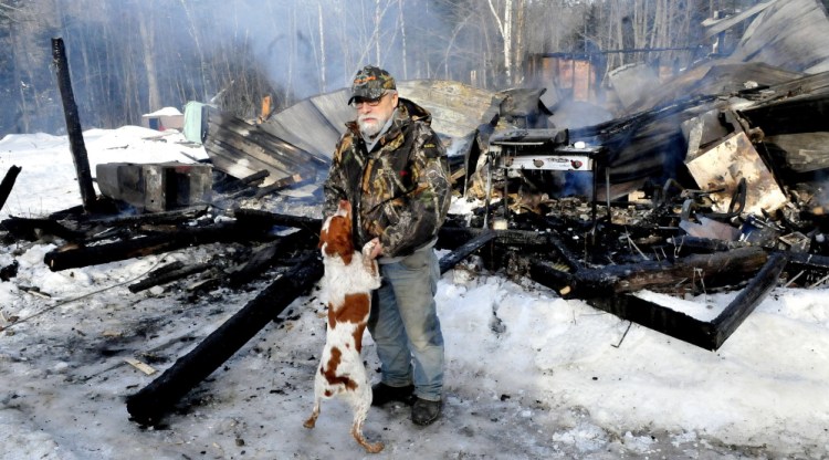 Homeowner Herb Hingley’s dog Babe jumps up on him beside his home that was destroyed by fire on the Rowe Pond Road in Pleasant Ridge on Wednesday. Hingley credited his dog with jumping on him and alerting him to the early morning fire.