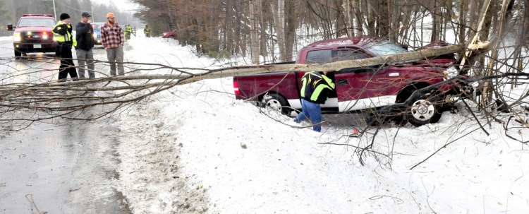 A man retrieves belongings from a pickup truck that slid off ice-covered Route 139 in Fairfield and snapped several trees early Sunday afternoon.