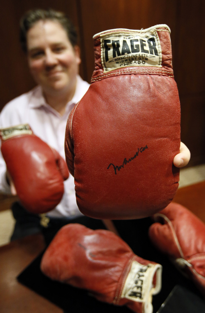 Chris Ivy, director of sports auctions at Heritage Auctions, holds the autographed gloves of Muhammad Ali with the gloves of Sonny Liston sitting on the table.