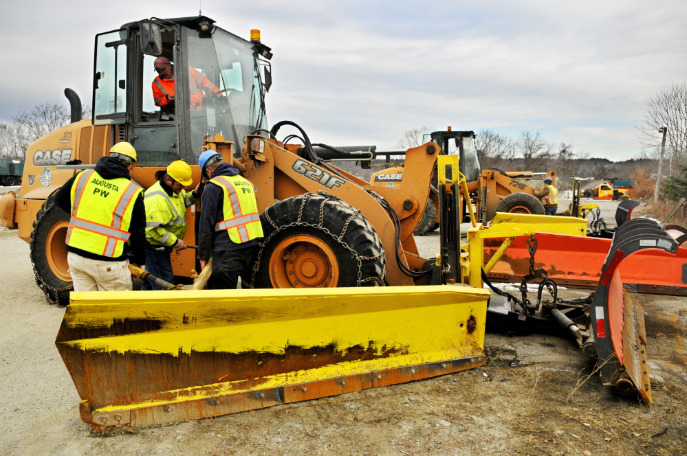 Workers swap from a scoop bucket to plow blades on front end loaders on Friday at the The John Charest Public Works Facility in Augusta.
