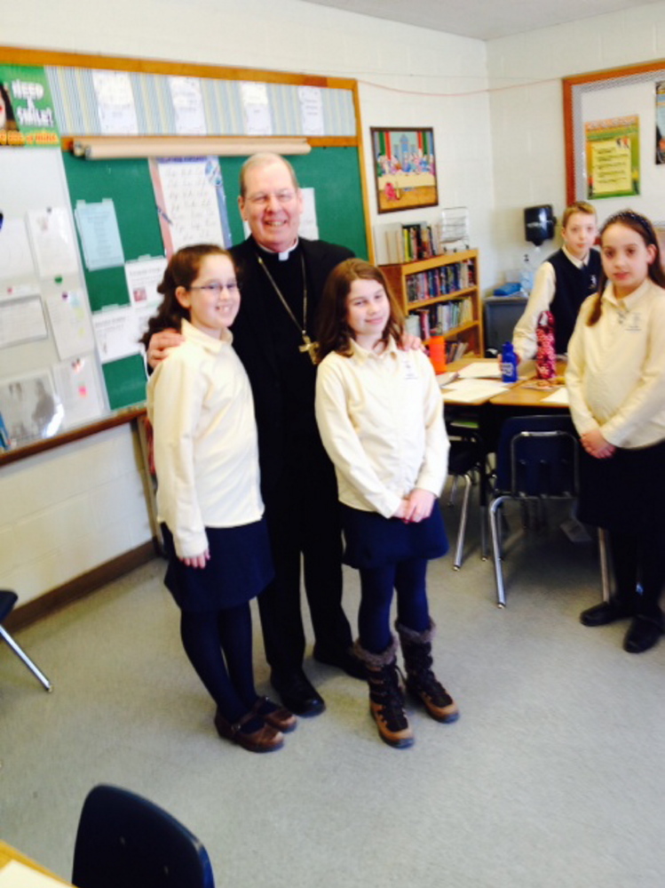 Plain Text:Bishop Robert Deeley meets with sixth grade student Dorothy Anne Giroux-Pare and Julia Bard during a visit to St. John Regional Catholic School in Winslow on Monday.