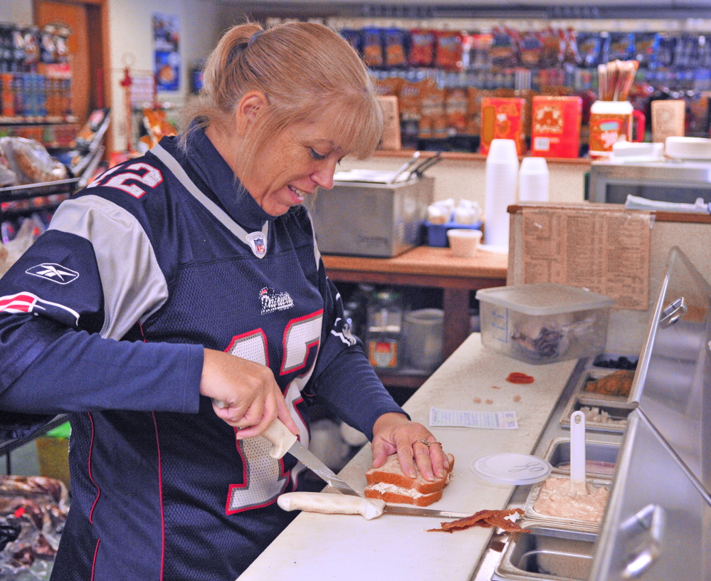 Carla Jenney wears a Tom Brady Patriots jersey while making sandwiches Saturday at College Carryout in Augusta.