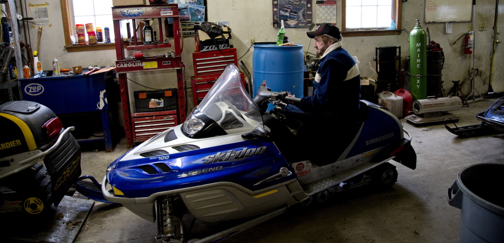 Wayne Keniston, owner of Keniston’s Auto & Snowmobile Supplies sits on a sled in his shop on the Gray Road in Falmouth on Monday. “It’s white gold for us.’ he said of Tuesday’s predicted snowfall.  