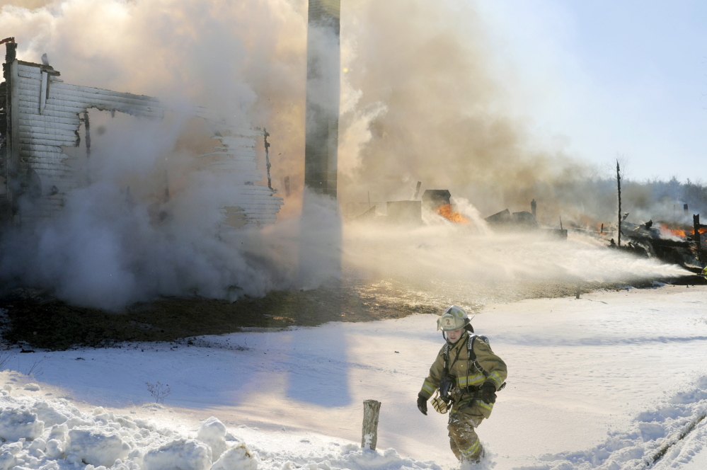 A firefighter climbs through a snowbank as a farmhouse is engulfed in flames on Route 105 in Somerville on Sunday.