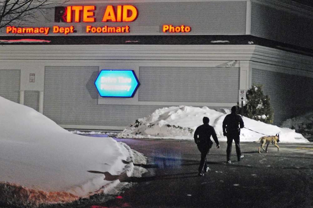 Two Augusta police officers and a tracking dog walk through the parking lot around 6:50 p.m. on Saturday after a robbery at the Rite Aid pharmacy at the corner of North Belfast Avenue and Bangor Street in Augusta.