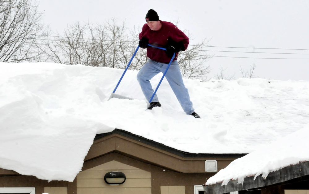 Mike MacDonald struggles against deep snow while shoveling off the roof of a building in Waterville on Monday. Homeowners are encouraged to reduce the weight of snow on buildings.
