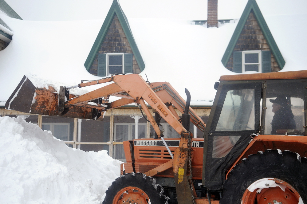 Jim Norton moves snowbanks Monday that have piled up under the eaves of the metal roof adorning his Farmingdale farmhouse. Norton said snow is yet to melt and slide off the center of his home because of overcast skies and cold weather.