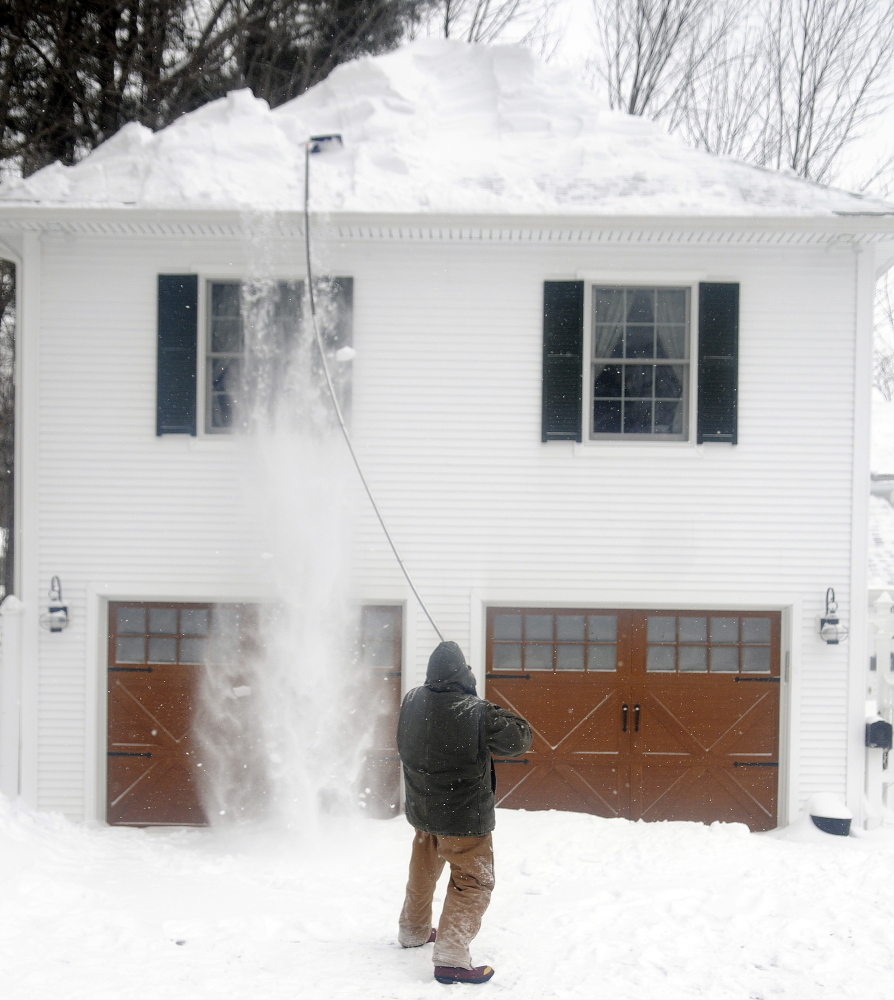 Pete Wilcox rakes snow off a home in Hallowell on Monday. The employee of Casco Bay Home Improvement cleaned the roof up after several inches of snow stacked up.