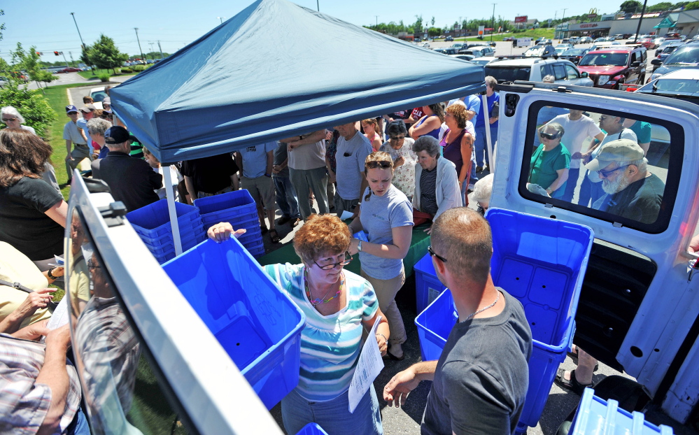 Ecomaine workers distribute free recycling bins to the public June 27, 2014, at Elm Plaza in Waterville. Ecomaine set up the event to hand out 100 free bins and information on the city’s recycling program. Augusta is considering a six-month trial program through Ecomaine.