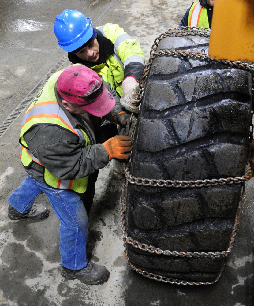 Donald Searles, top, and Pete Porter mount a chain on front end loader tire on Friday at the John Charest Public Works facility in Augusta. Public works staffers spent part of their Friday shifts preparing equipment for the storm forecast to hit the area this weekend.