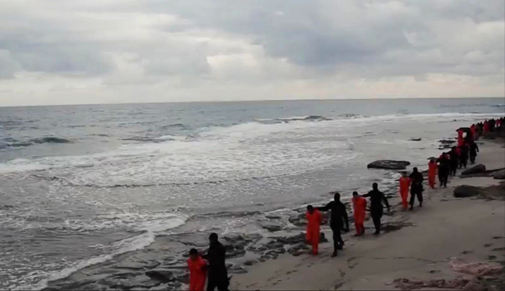 This image made from a video released Sunday by militants in Libya claiming loyalty to the Islamic State group purportedly shows Egyptian Coptic Christians in orange jumpsuits being led along a beach, each accompanied by a masked militant.