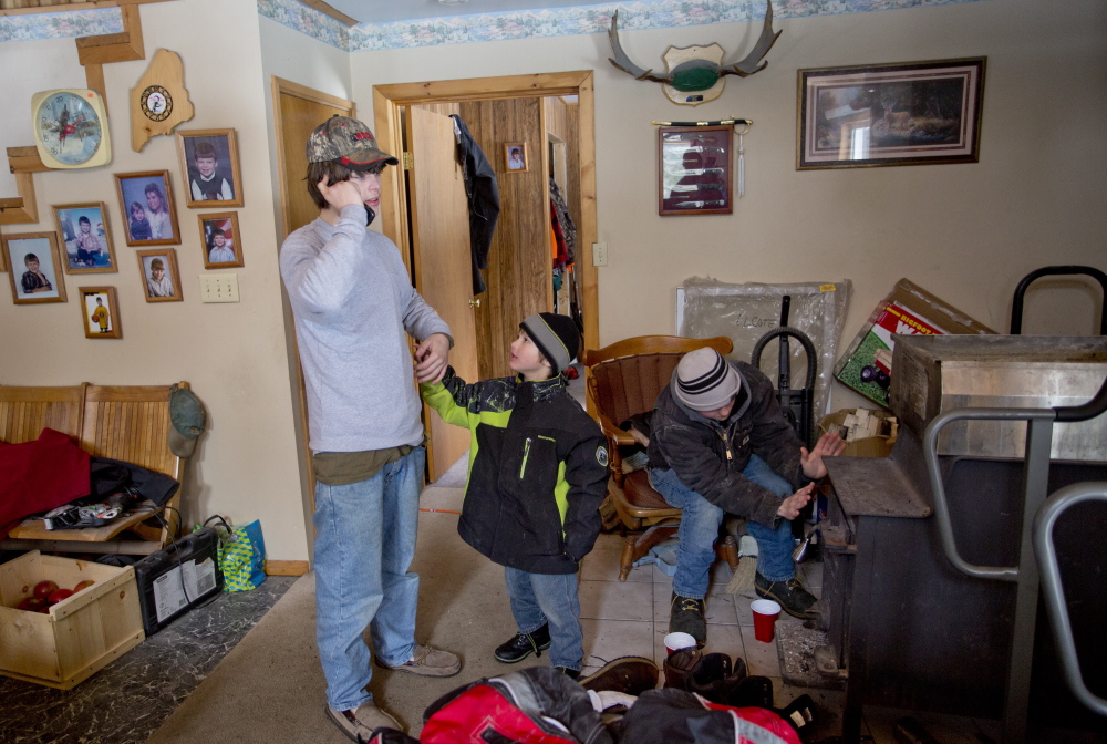 AT LEFT: Tyler Howard-Gotto talks on the phone with a reporter while his brother, Gauge Howard-Fowler, 4, tries to get his attention and friend Jonah May warms his hands by the wood stove at the camp owned by Tyler’s grandfather in Andover.