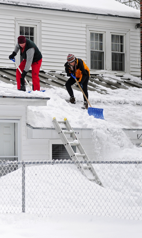 Tom Towle, left, and Debi Towle shovel off a roof on Thursday after an overnight snowstorm in Augusta.