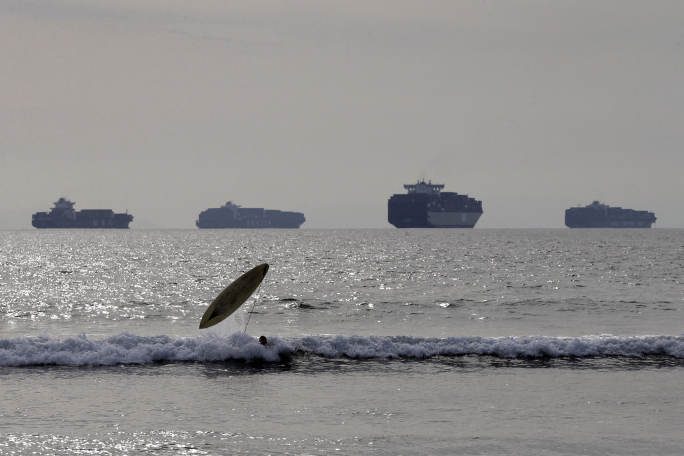 Jake Ferguson loses his surfboard while riding a wave, Friday, in Sunset Beach, Calif., as loaded cargo ships are anchored outside the Ports of Long Beach and Los Angeles.