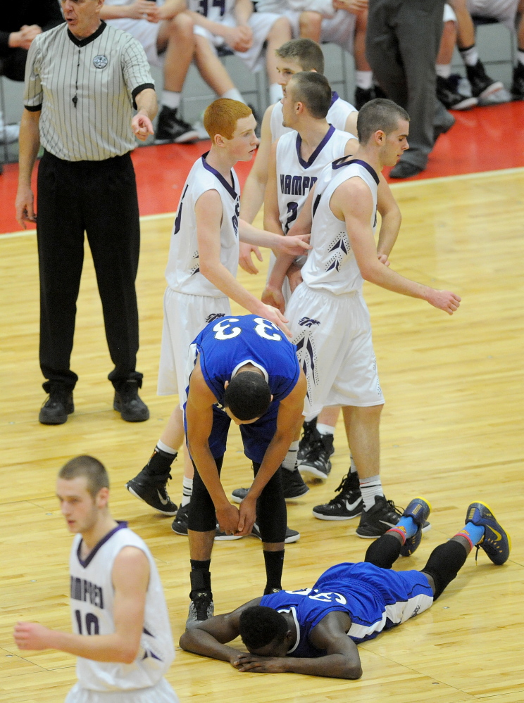 Lewiston High School’s Quintarian Brown, 30, lies on the court as his teammate Isaiah Harris, 33, tries to help him up after fouling Hampden Academy’s Nick Gilpin, 4, late in the fourth quarter of the Eastern A final on Saturday.