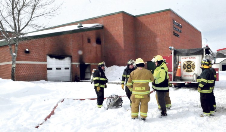 Firefighters from Vassalboro and Winslow wait as the Vassalboro Community School is ventilated of black smoke after a tractor caught on fire inside the attached garage, background, that caused substantial damage on Sunday