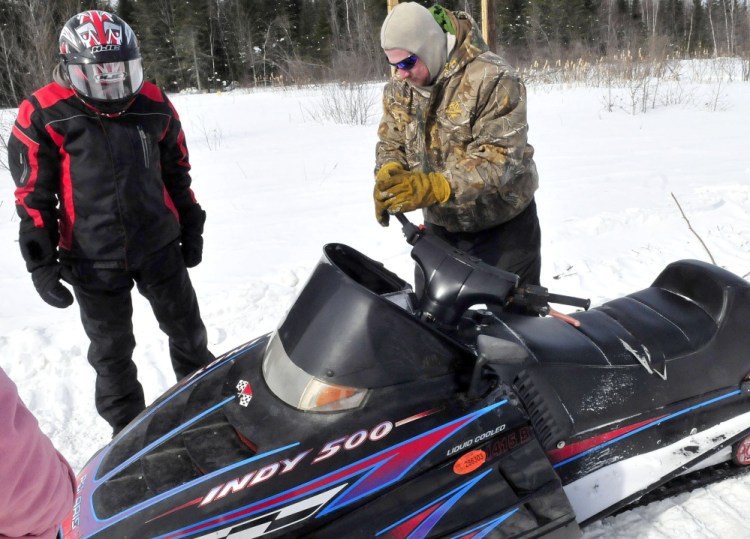 Patrick LaGross, right, of the Clinton Snowmobile club, turns the twisted steering wheel of the snowmobile on which Brittany Wentworth of Clinton was involved in an accident on a trail near Johnson Flat Road in Winslow. At left is Matt Lee of the Benton Snowmobile club, which towed the disabled snowmobile. Lee accompanied Wentworth on the snowmobiling trip and took her on his machine to meet rescue workers on the road.
