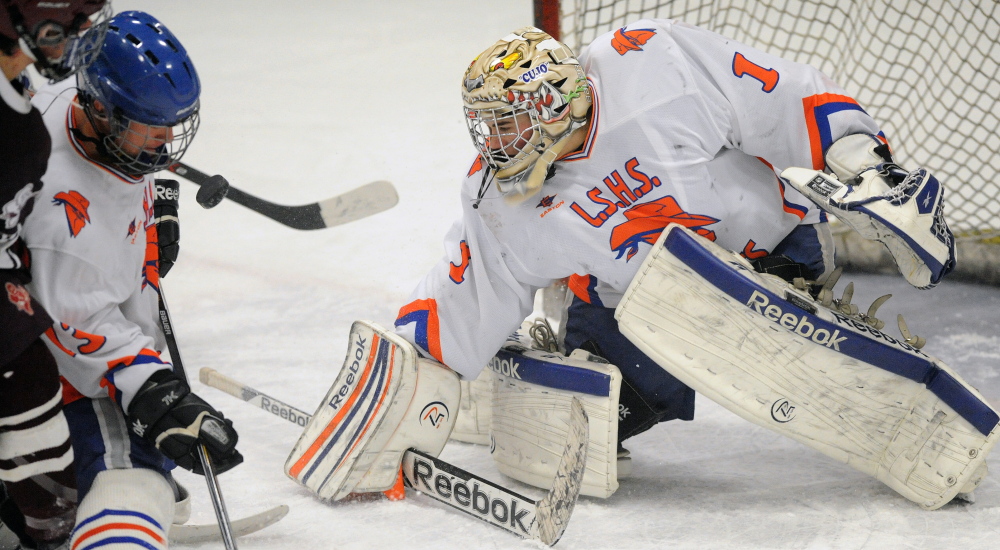 Staff photo by Michael G. Seamans 
 The puck hovers in front of Lawrence/Skowhegan High School's Samuel Haver (13) as goalie Curtis Martin (1) tries to make the save during an Eastern A quarterfinal Tuesday night at Sukee Arena.