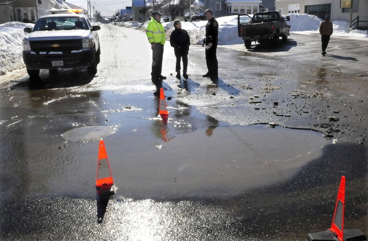 Motorist Muriel Rancourt, center, speaks with Winslow Public Works Director Paul Fongemie, left, and officer John Veilleux after her car drove over a water-filled sinkhole beside Monument Street on Wednesday. The hole, three to four feet deep,  was created by a broken water line on Clinton Avenue. “I couldn’t believe it when I hit that,” Rancourt said while waiting for a tow truck. Fongemie said at least six vehicles hit the hole, leaving several with flat tires. The street was closed to traffic Wednesday afternoon while crews from Kennebec Water District repaired the broken pipe.